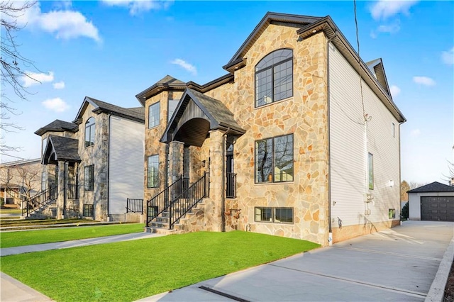 view of front of property featuring a detached garage, stone siding, an outdoor structure, driveway, and a front lawn