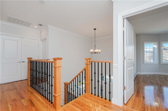 stairway with hardwood / wood-style floors, ornamental molding, and an inviting chandelier