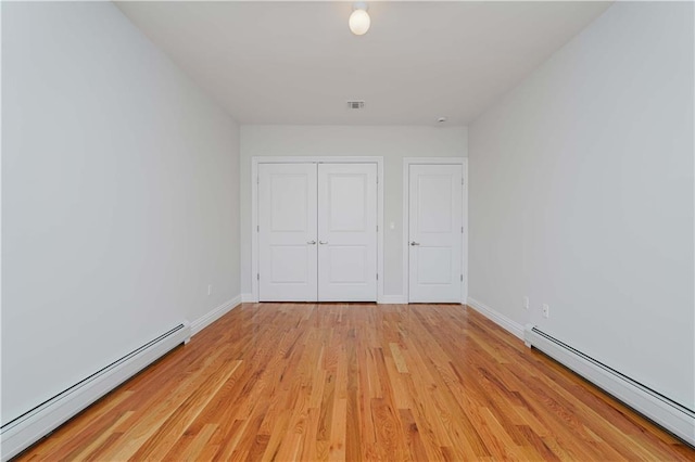 unfurnished bedroom featuring a baseboard heating unit, a closet, and light hardwood / wood-style flooring