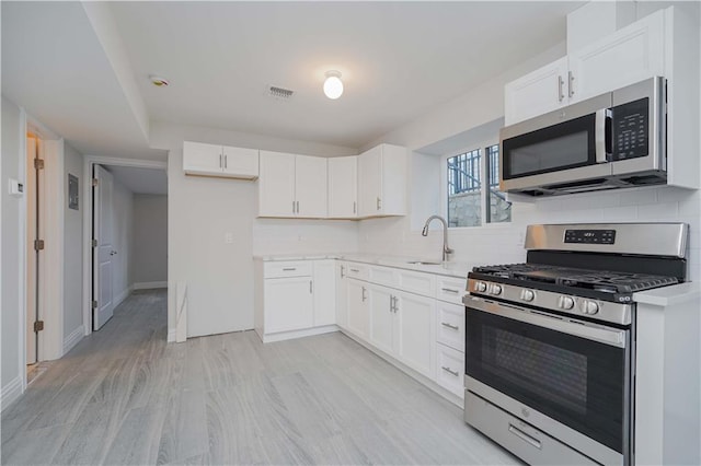 kitchen with white cabinetry, stainless steel appliances, decorative backsplash, sink, and light hardwood / wood-style flooring