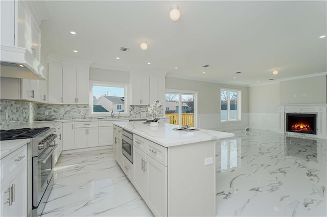 kitchen featuring light stone countertops, white cabinets, appliances with stainless steel finishes, a kitchen island, and ventilation hood