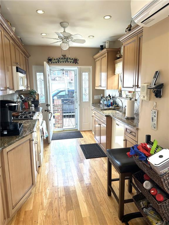 kitchen with sink, a wall mounted AC, light wood-type flooring, stone counters, and white appliances