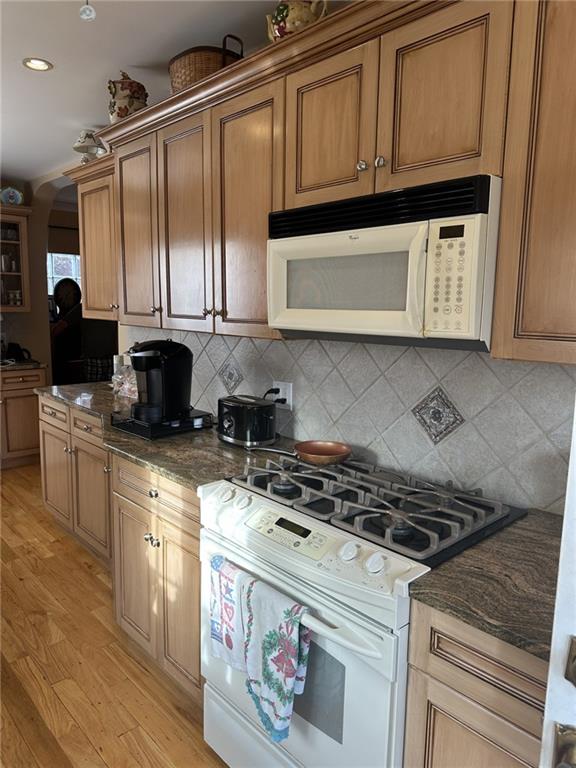 kitchen featuring white appliances, light hardwood / wood-style floors, decorative backsplash, and dark stone countertops