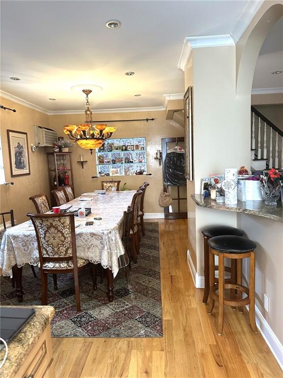 dining room with a notable chandelier, a wall mounted air conditioner, light hardwood / wood-style flooring, and ornamental molding