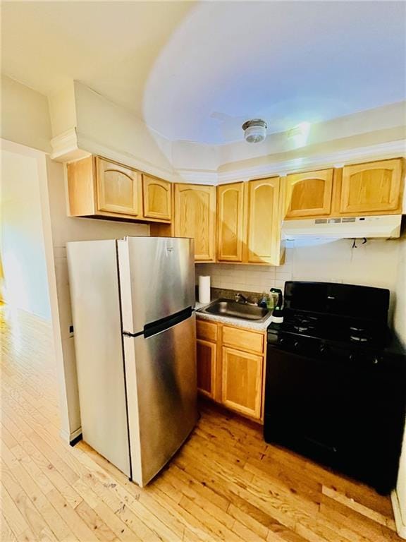 kitchen with freestanding refrigerator, light countertops, under cabinet range hood, a sink, and gas stove