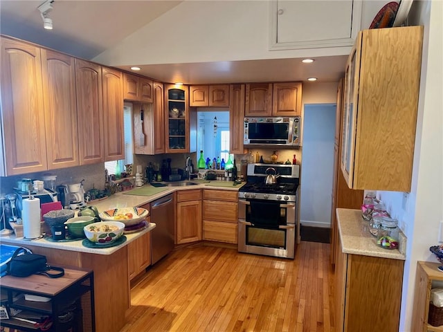 kitchen featuring backsplash, appliances with stainless steel finishes, light wood-type flooring, and vaulted ceiling