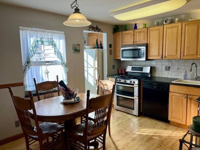 kitchen with a sink, backsplash, dark countertops, stainless steel appliances, and light wood finished floors