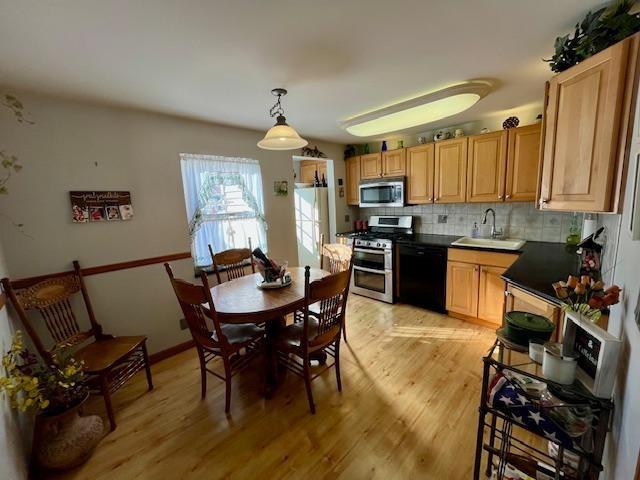 kitchen featuring stainless steel appliances, sink, light hardwood / wood-style floors, backsplash, and pendant lighting