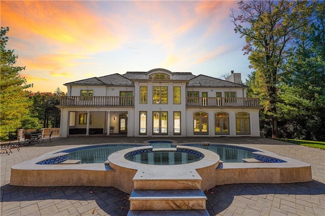 back house at dusk featuring a patio, a balcony, and a pool with hot tub