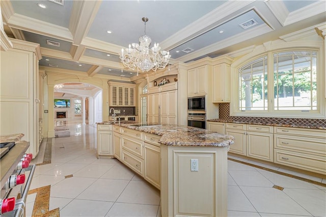 kitchen with coffered ceiling, black appliances, an island with sink, cream cabinetry, and decorative light fixtures