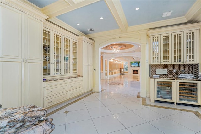 kitchen featuring beverage cooler, beamed ceiling, crown molding, cream cabinetry, and light tile patterned floors