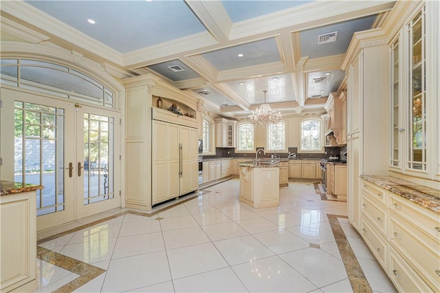 kitchen featuring cream cabinets, a kitchen island with sink, french doors, and hanging light fixtures