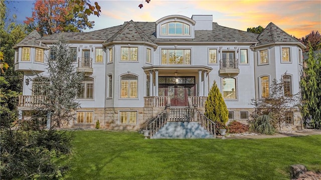 back of property at dusk featuring stairs, a yard, stucco siding, and french doors