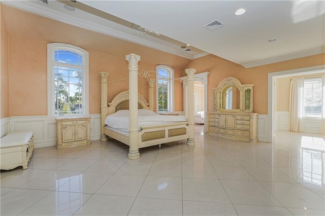 bedroom with a decorative wall, wainscoting, light tile patterned floors, visible vents, and crown molding