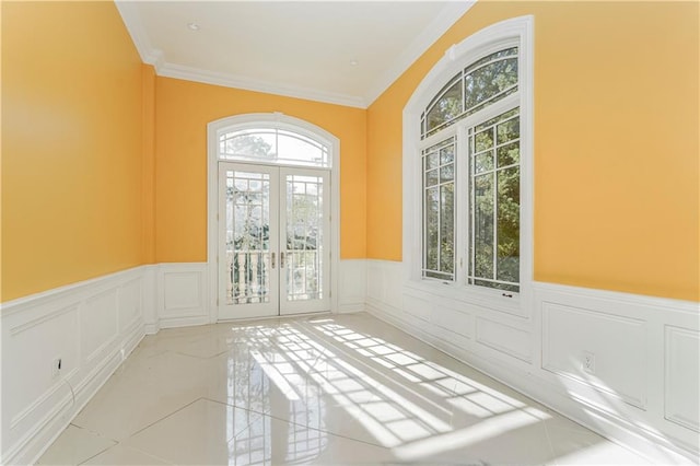 spare room featuring a wainscoted wall, french doors, crown molding, and a decorative wall