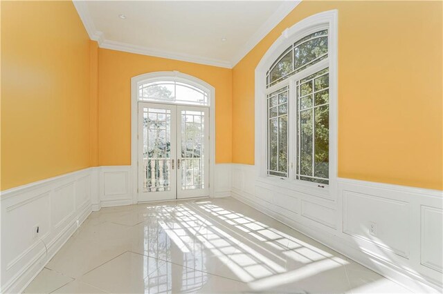 empty room featuring a decorative wall, french doors, a wainscoted wall, and ornamental molding