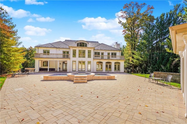 back of house featuring a balcony, an in ground hot tub, and a patio