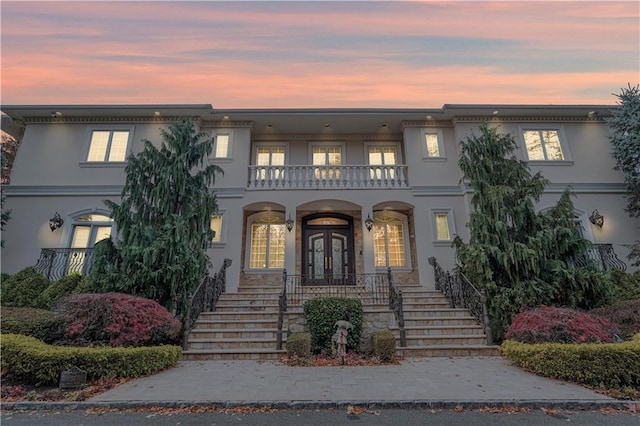 view of front facade featuring a balcony, stucco siding, stairway, a porch, and french doors