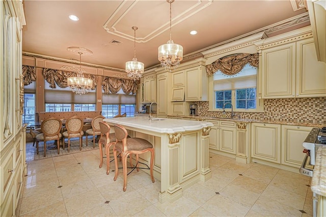 kitchen featuring sink, a center island with sink, pendant lighting, cream cabinets, and decorative backsplash