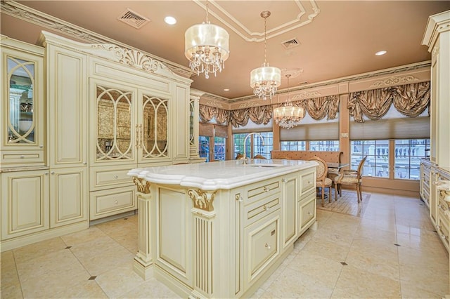 kitchen with sink, a kitchen island with sink, cream cabinets, and hanging light fixtures