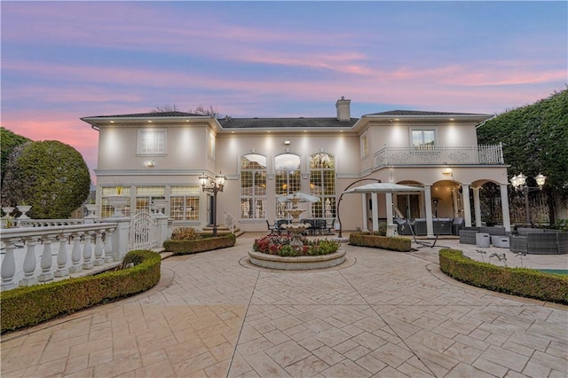 back of house featuring a balcony, a patio, a chimney, outdoor lounge area, and stucco siding