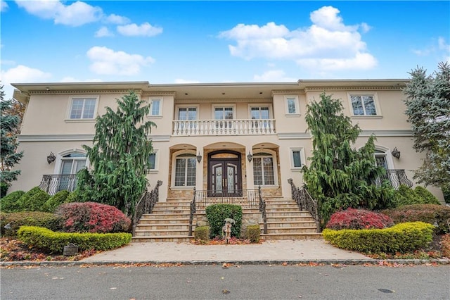 view of front of home with a balcony, stucco siding, stairway, a porch, and french doors