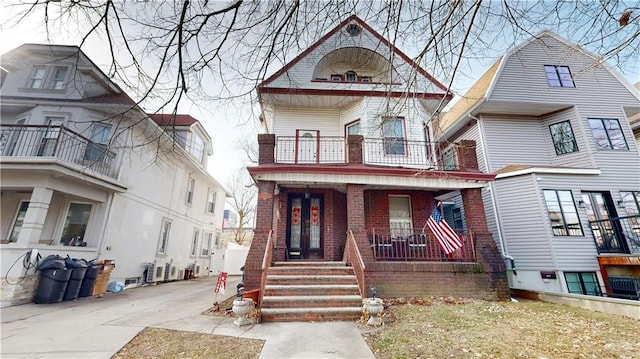 victorian home featuring covered porch, brick siding, and a balcony