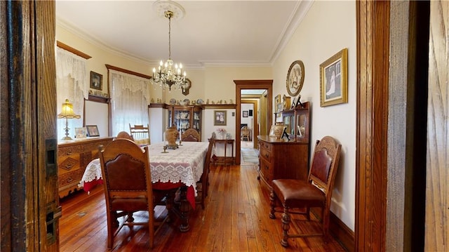 dining area with dark wood-type flooring, ornamental molding, and a notable chandelier