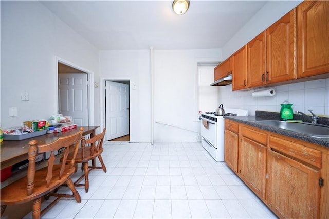 1830 81st St, Brooklyn, NY 11214 - kitchen with under cabinet range hood, dark countertops, a sink, brown cabinetry, and white range with gas cooktop