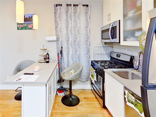 kitchen featuring stainless steel appliances, white cabinetry, a kitchen breakfast bar, light wood-type flooring, and hanging light fixtures