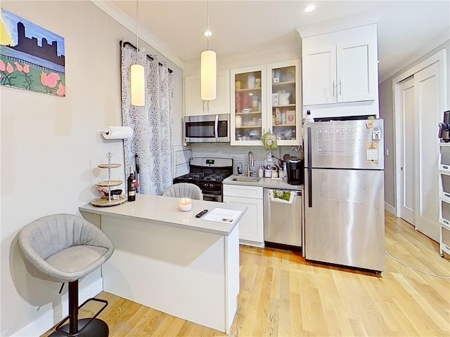 kitchen with pendant lighting, light wood-type flooring, white cabinetry, appliances with stainless steel finishes, and sink