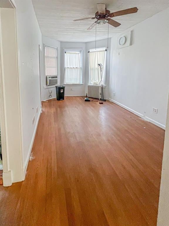 empty room featuring radiator heating unit, light wood-type flooring, ceiling fan, and cooling unit