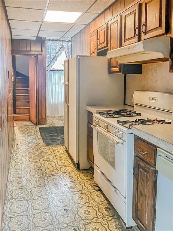 kitchen with white appliances, a paneled ceiling, and wood walls