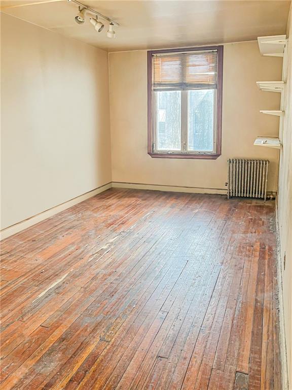 unfurnished room featuring rail lighting, radiator, and hardwood / wood-style floors