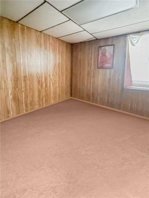 carpeted empty room featuring wood walls and a drop ceiling