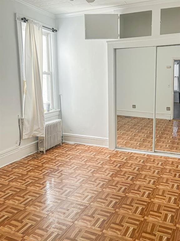 unfurnished bedroom with a closet, crown molding, radiator heating unit, and light parquet floors