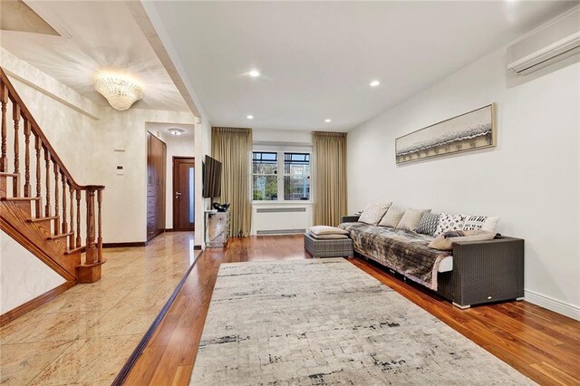 living room featuring an inviting chandelier, a wall mounted air conditioner, and light hardwood / wood-style flooring