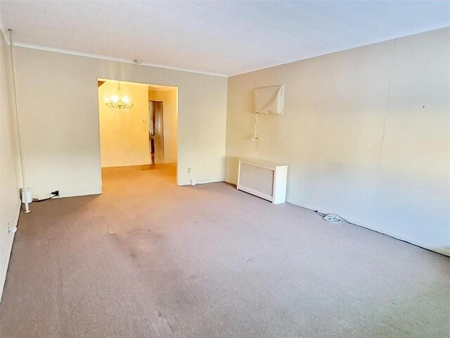 empty room with an inviting chandelier, ornamental molding, radiator heating unit, and carpet