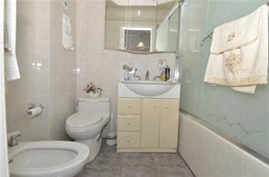 full bath with toilet, combined bath / shower with glass door, vanity, a bidet, and tile walls