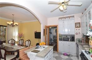 kitchen with arched walkways, light countertops, ceiling fan with notable chandelier, and white cabinetry