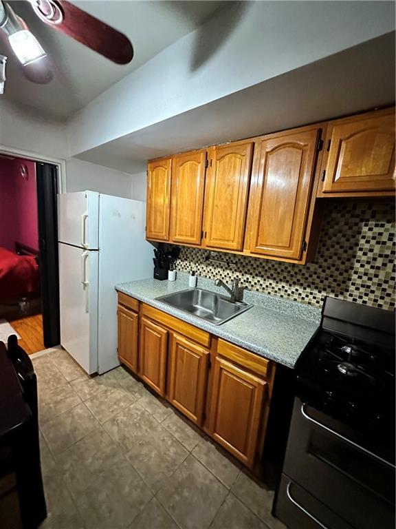 kitchen featuring ceiling fan, decorative backsplash, sink, stainless steel gas stove, and white refrigerator