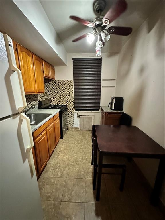 kitchen with black stove, white refrigerator, decorative backsplash, sink, and ceiling fan