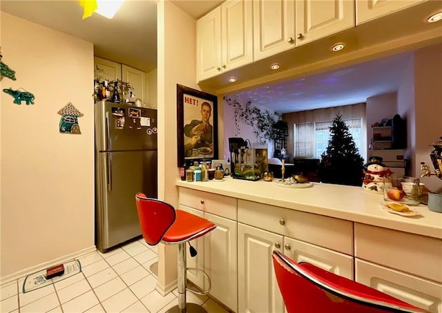 bar featuring light tile patterned floors, stainless steel refrigerator, and white cabinetry