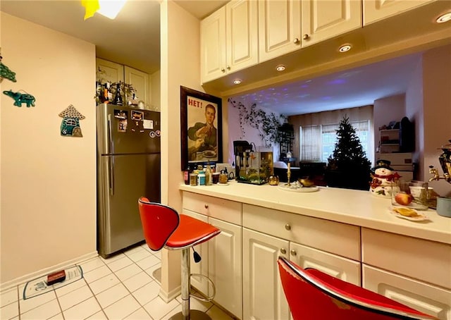 kitchen with freestanding refrigerator, light tile patterned flooring, baseboards, light countertops, and white cabinetry