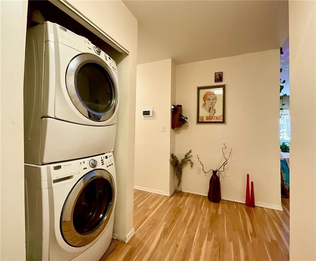 clothes washing area featuring baseboards, laundry area, stacked washer / dryer, and light wood-style floors