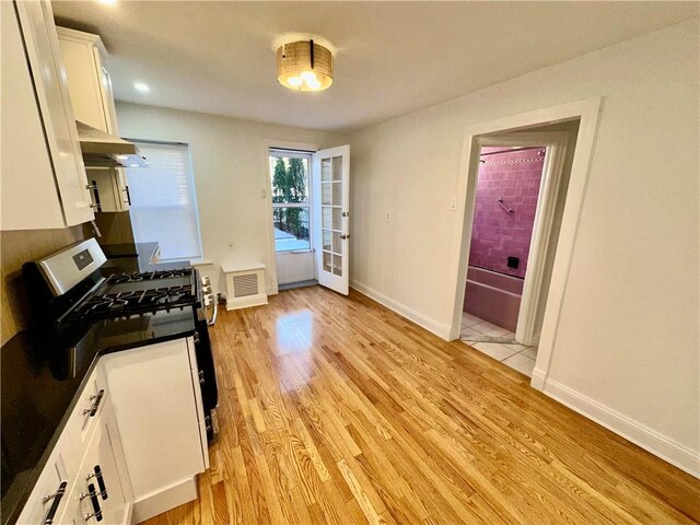 kitchen with stainless steel range with gas cooktop, range hood, light hardwood / wood-style flooring, and white cabinets