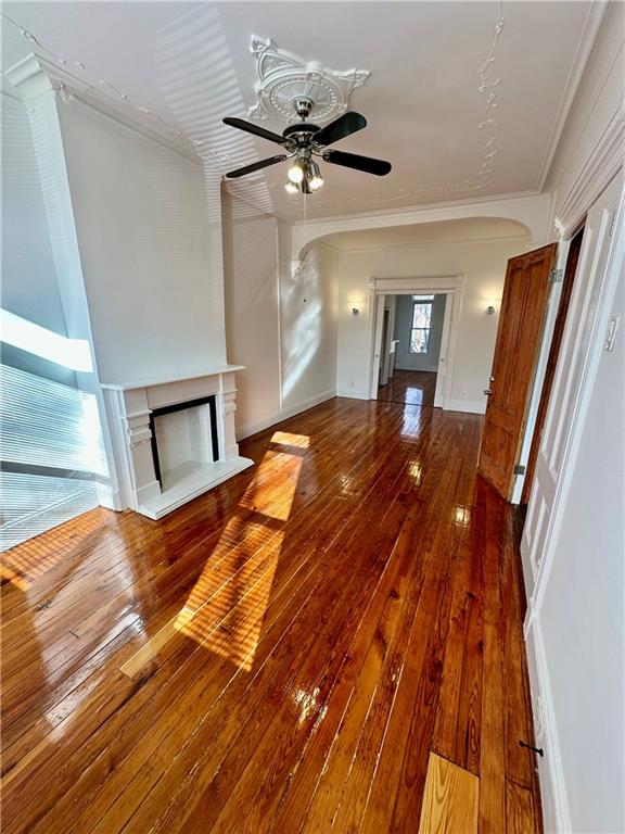 unfurnished living room with ceiling fan, crown molding, a fireplace with raised hearth, and hardwood / wood-style floors