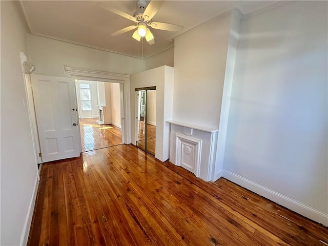 unfurnished living room with wood-type flooring, baseboards, ceiling fan, and crown molding