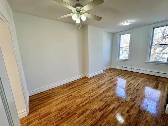 spare room featuring baseboard heating, wood-type flooring, a ceiling fan, and baseboards