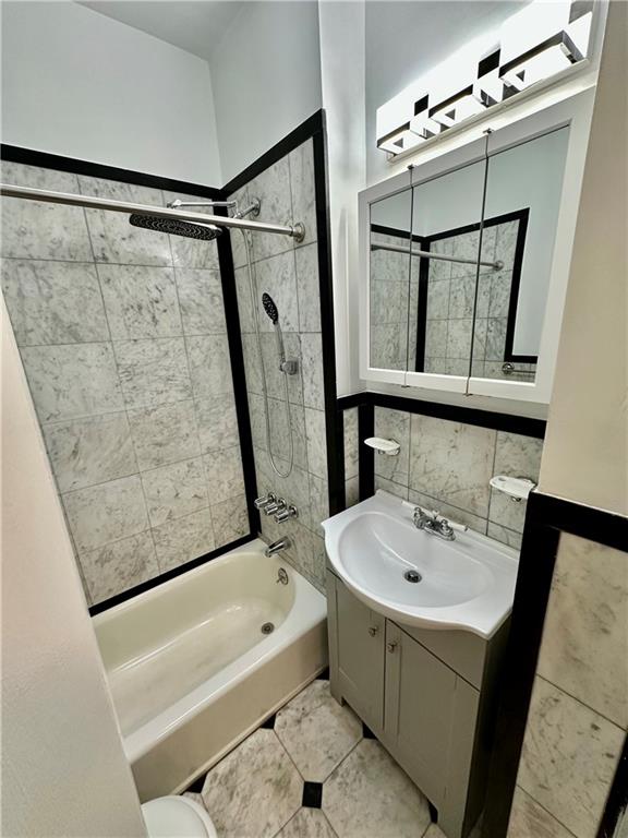 bathroom with tile walls, tile patterned flooring, tiled shower / bath combo, and vanity